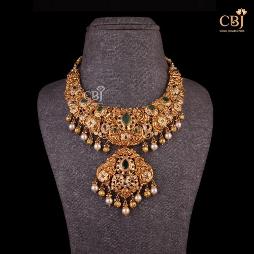 Crafted with precision, a gold statement necklace studded with emerald, CZ and pearls.