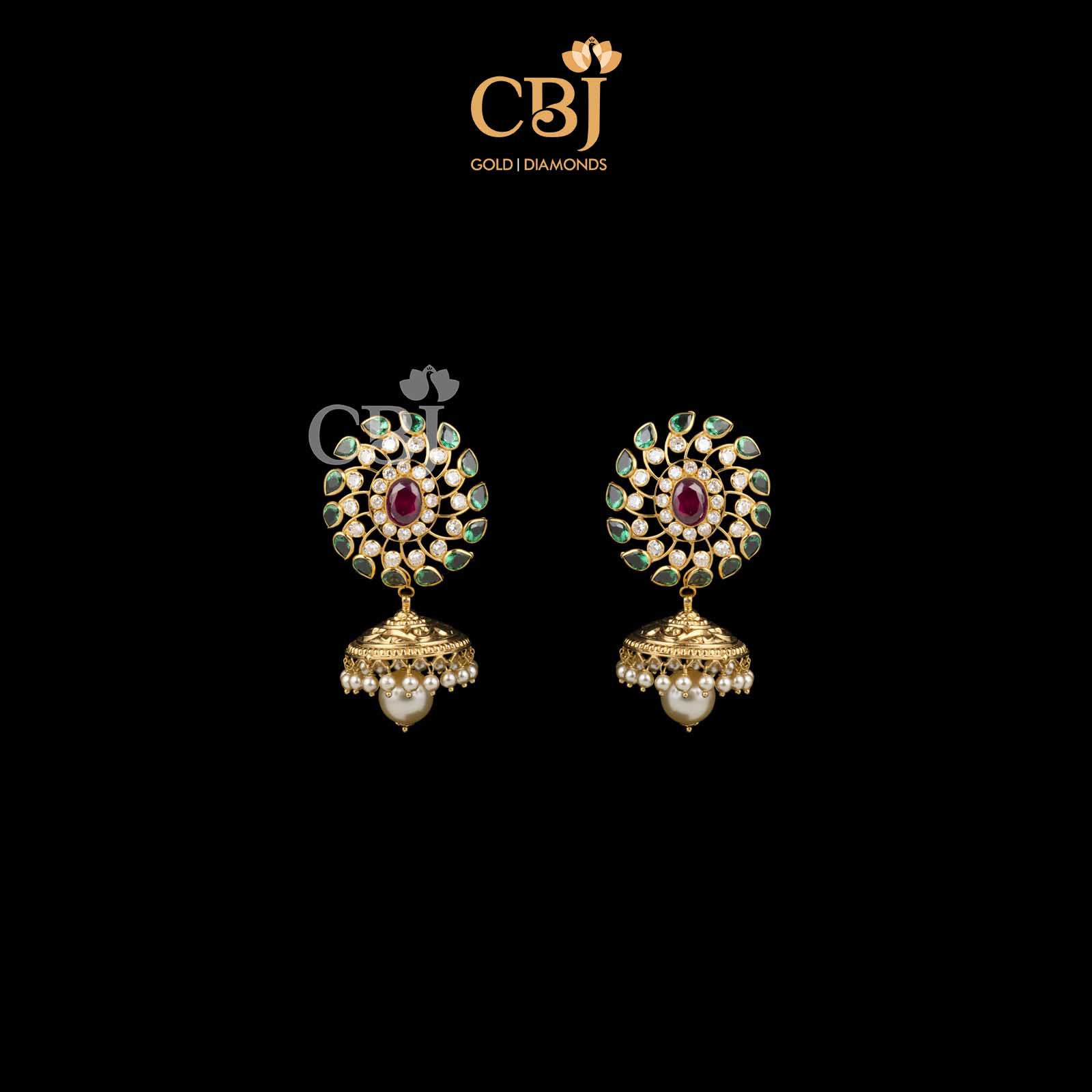 Glow in green with the charm casted by the emerald stones in this stunning set of jhumkas.