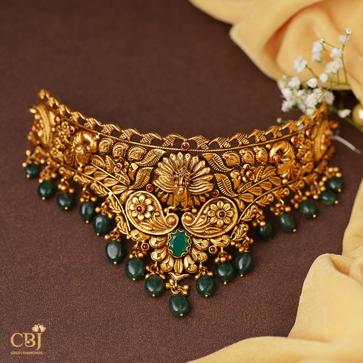 A perfect antique choker that can compliment your grace and elegance. An opulent design with suspended emerald drops.  Mayura Nakashi Choker with Emerald Drops.