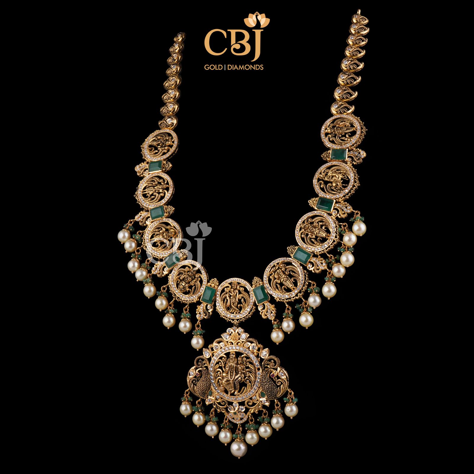 This stunning Dasavataram Semi long haram is an incredible marvel in design featuring emerald stones and suspended pearl drops.