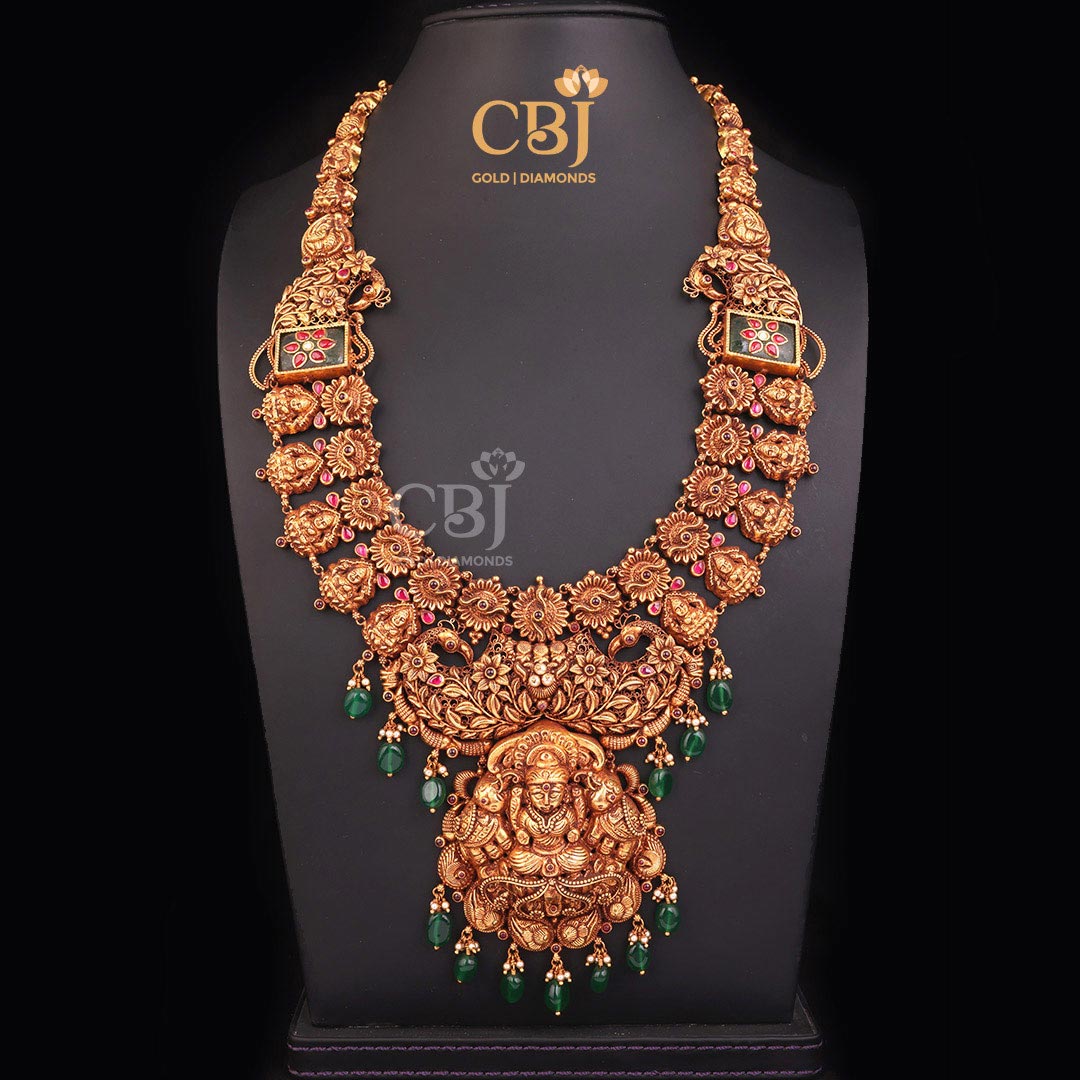 An intricate long Gajalakshmi haram featuring emerald stones.