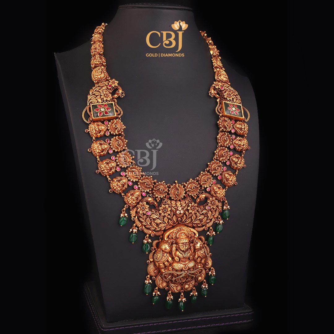 An intricate long Gajalakshmi haram featuring emerald stones.